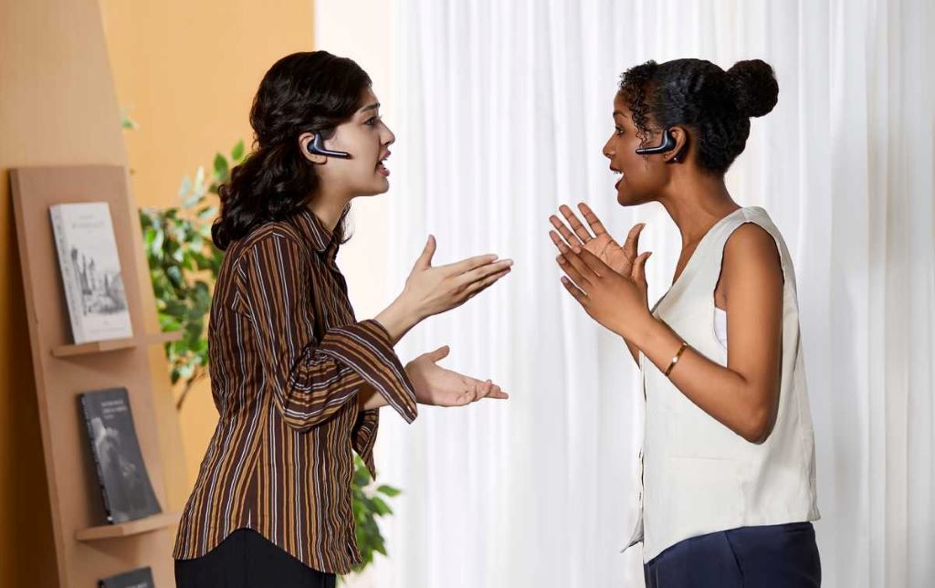 A person wearing translator earbuds while having a conversation with someone speaking a different language in a bustling city