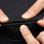 Close-up of hands inspecting wetsuit seam for leaks and damage