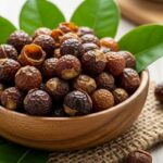 Dried soap nut shells in a wooden bowl with fresh green leaves on natural background showing sustainable personal hygiene products