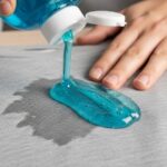 Person applying dish soap to oil-stained clothing fabric for pre-treatment before washing