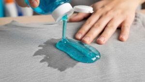 Person applying dish soap to oil-stained clothing fabric for pre-treatment before washing