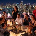Sophisticated adults enjoying cocktails at upscale Miami rooftop lounge with city skyline view at night