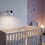 Modern smart baby monitor camera positioned above a crib in a softly lit nursery room