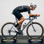 Cyclist riding on bike rollers demonstrating balance and proper form during indoor training session with three-drum roller setup