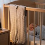 Digital room thermometer displaying 68 degrees next to baby crib with sleep sack hanging nearby for safe winter sleep temperature monitoring