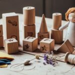 Handmade wooden toy blocks and soft fabric doll made from natural organic materials arranged on a wooden table with craft supplies