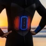Surfer wearing battery powered wetsuit with rechargeable battery pack attached, demonstrating proper fit and heating system placement for cold water surfing