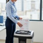 Office worker using cross-cut shredder to destroy confidential business documents according to DIN security standards