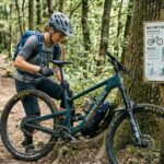 A mountain biker adjusting saddle height on a trail bike next to a sizing chart