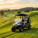 Modern electric golf cart driving up a steep green fairway slope.