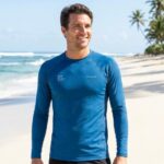 Man wearing a blue UV protection surf shirt on a sunny beach.