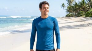 Man wearing a blue UV protection surf shirt on a sunny beach.